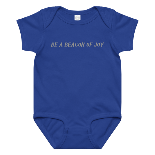 "Be a beacon of joy" printed on a royal baby jersey bodysuit laying on a flat surface amongst other clothes
