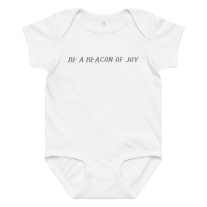 "Be a beacon of joy" printed on a white baby jersey bodysuit laying on a flat surface amongst other clothes