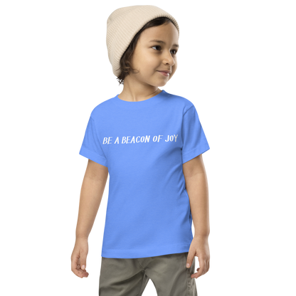 "Be a beacon of joy" printed on a heather columbia blue toddler short sleeve tee worn by a male wearing a cap