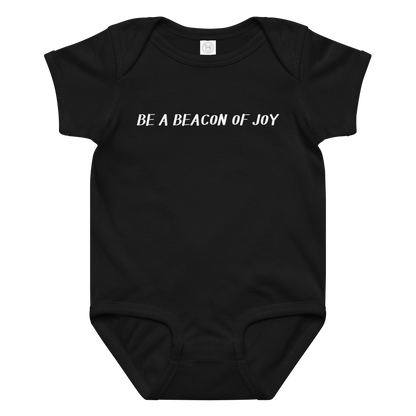 "Be a beacon of joy" printed on a black baby jersey bodysuit laying on a flat surface amongst other clothes