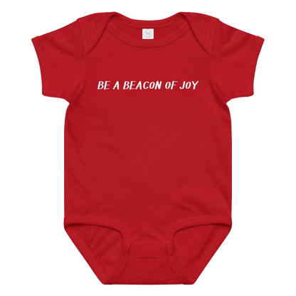 "Be a beacon of joy" printed on a red baby jersey bodysuit laying on a flat surface amongst other clothes