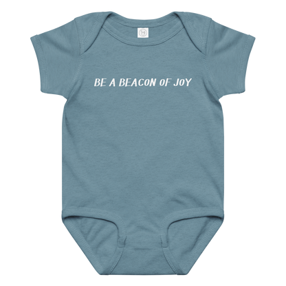 "Be a beacon of joy" printed on a vintage indigo baby jersey bodysuit laying on a flat surface amongst other clothes