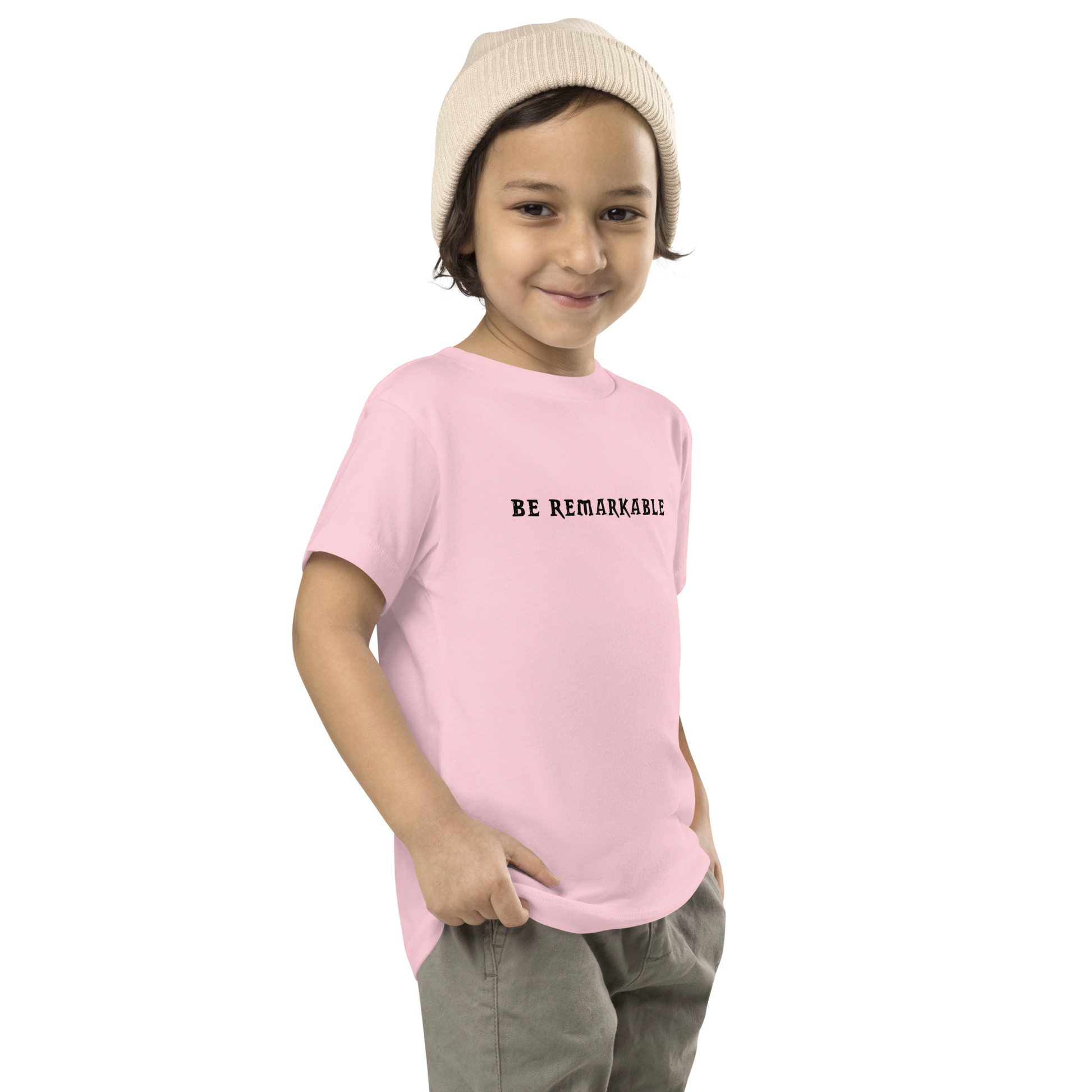 "Be remarkable" printed on a pink toddler short sleeve tee worn by a male who is also wearing a knit cap