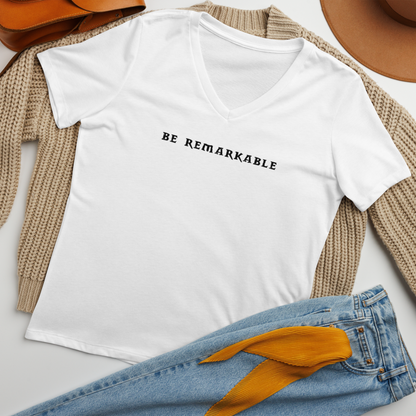 "Be remarkable" printed on a solid white blend women's relaxed v-neck t-shirt laying on a flat surface amongst other clothes
