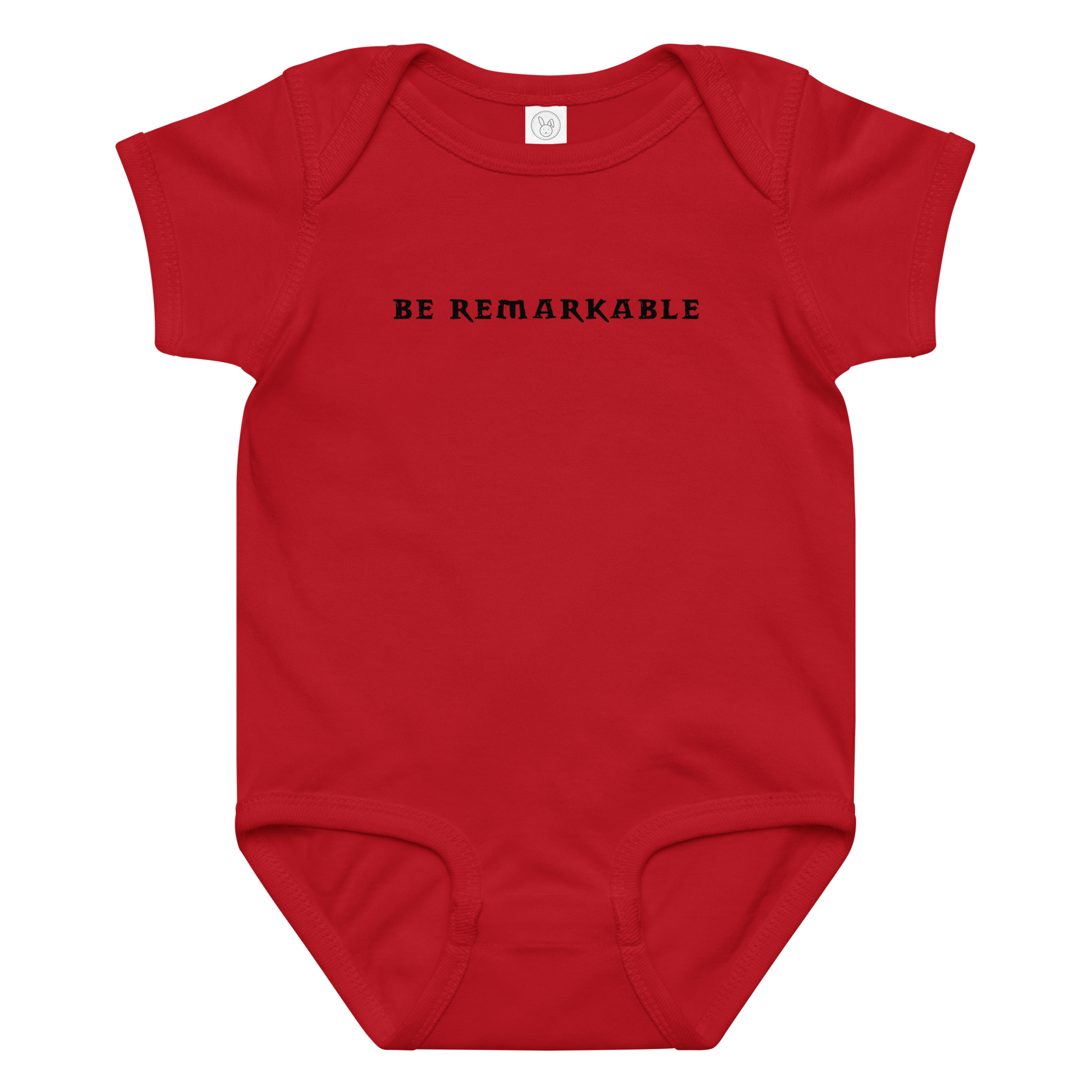 "Be remarkable" printed on a red baby jersey bodysuit laying on a flat surface amongst other clothes