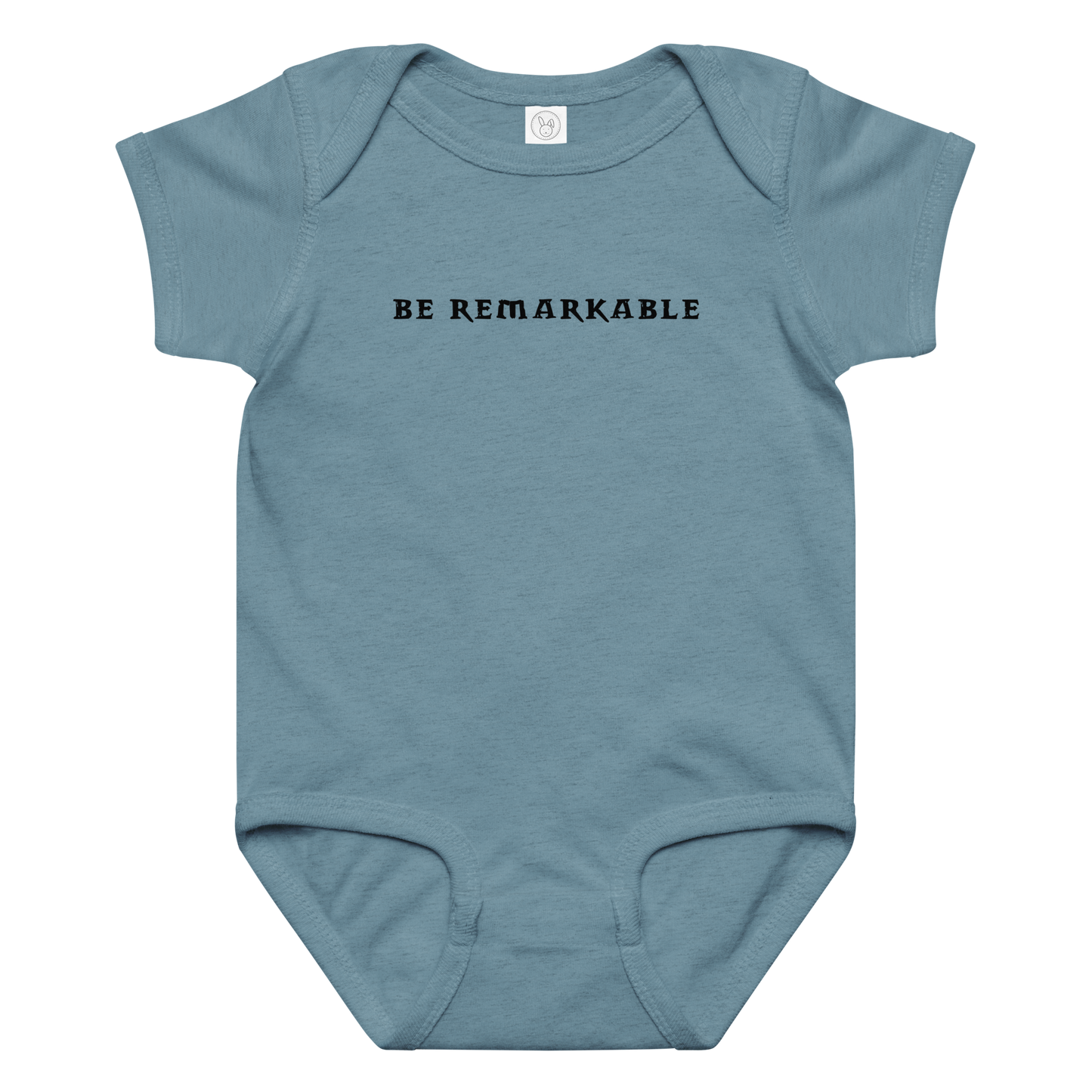 "Be remarkable" printed on a vintage indigo baby jersey bodysuit laying on a flat surface amongst other clothes