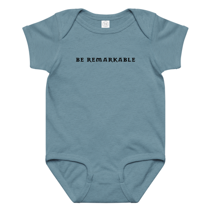 "Be remarkable" printed on a vintage indigo baby jersey bodysuit laying on a flat surface amongst other clothes