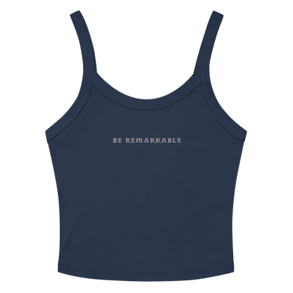 "Be remarkable" printed on a solid navy blend women's micro-rib tanktop laying on a flat surface amongst sunglasses and shorts