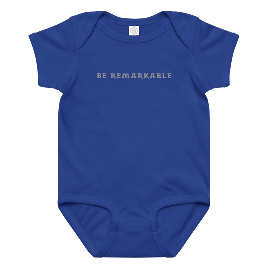 "Be remarkable" printed on a royal baby jersey bodysuit laying on a flat surface amongst other clothes