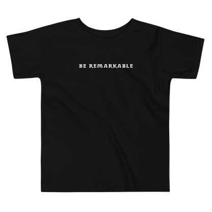 "Be remarkable" printed on a black toddler short sleeve tee laying on a flat surface