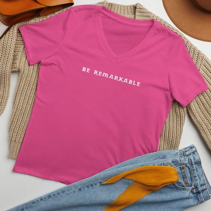 "Be remarkable" printed on a berry women's relaxed v-neck t-shirt laying on a flat surface amongst other clothes