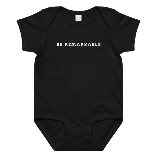 "Be remarkable" printed on a black baby jersey bodysuit laying on a flat surface amongst other clothes