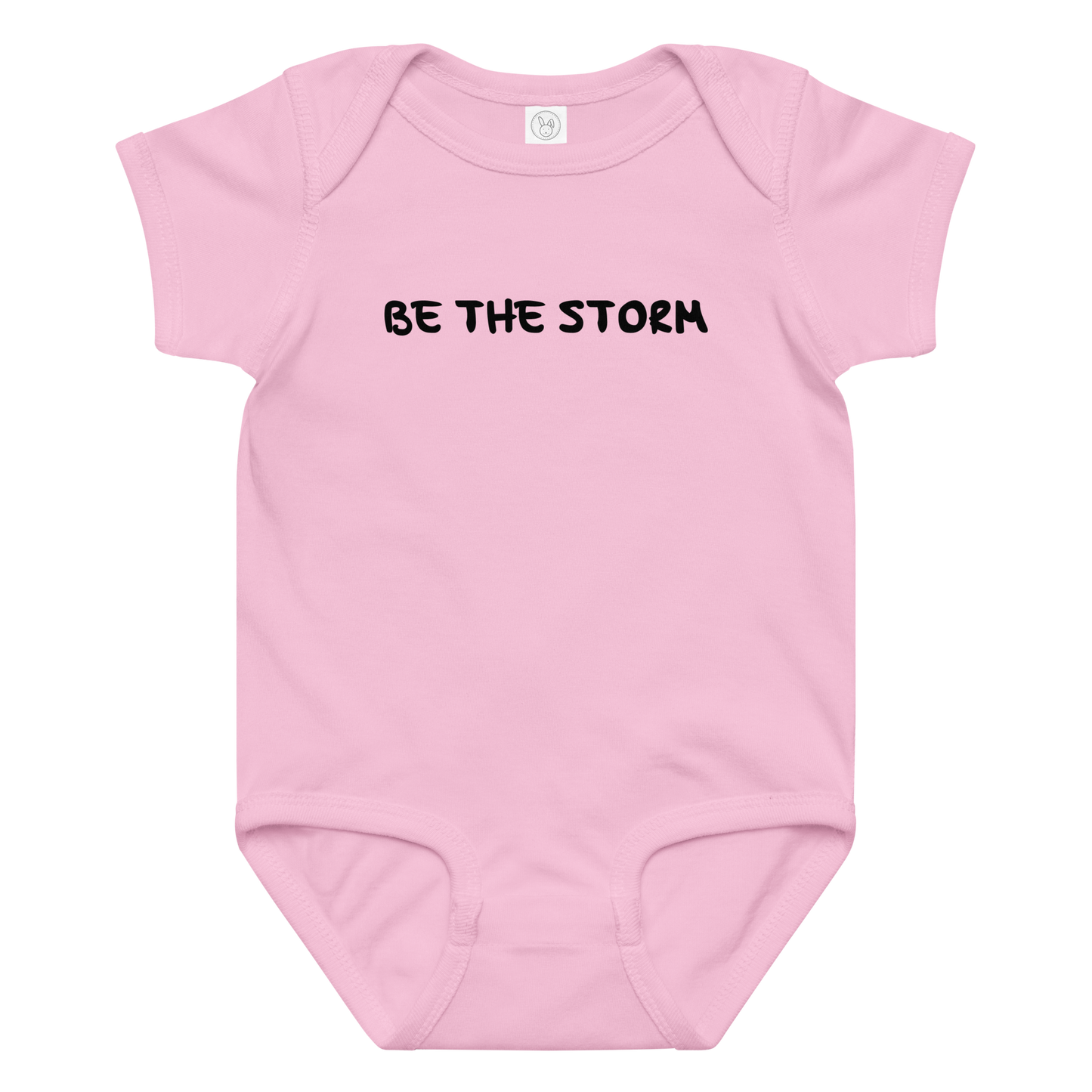 "Be the storm" printed on a pink baby jersey bodysuit laying on a flat surface amongst other clothes