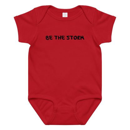 "Be the storm" printed on a red baby jersey bodysuit laying on a flat surface amongst other clothes