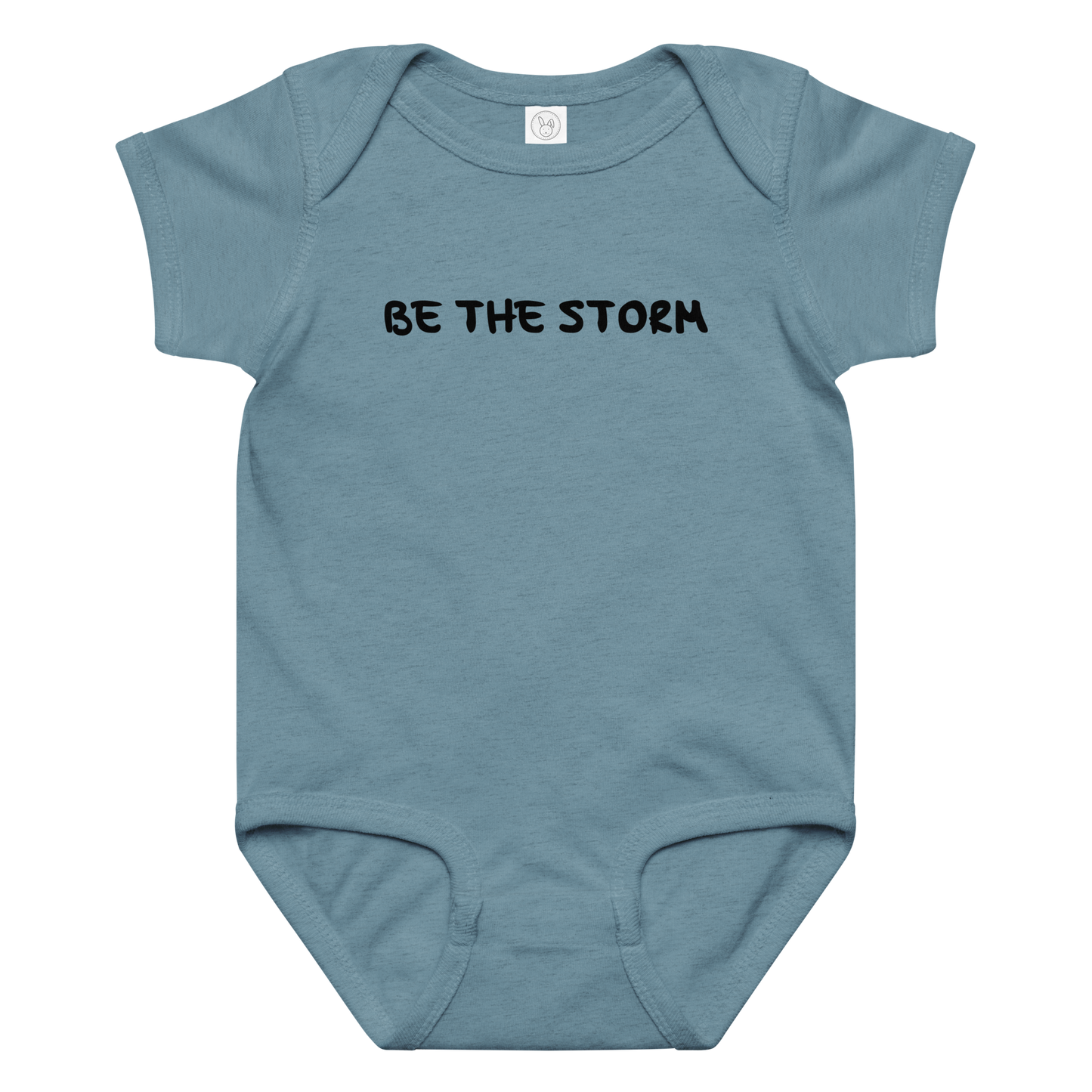"Be the storm" printed on a vintage indigo baby jersey bodysuit laying on a flat surface amongst other clothes