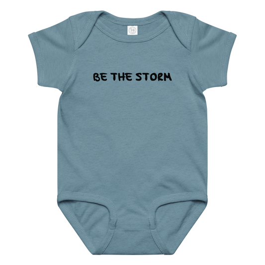 "Be the storm" printed on a vintage indigo baby jersey bodysuit laying on a flat surface amongst other clothes