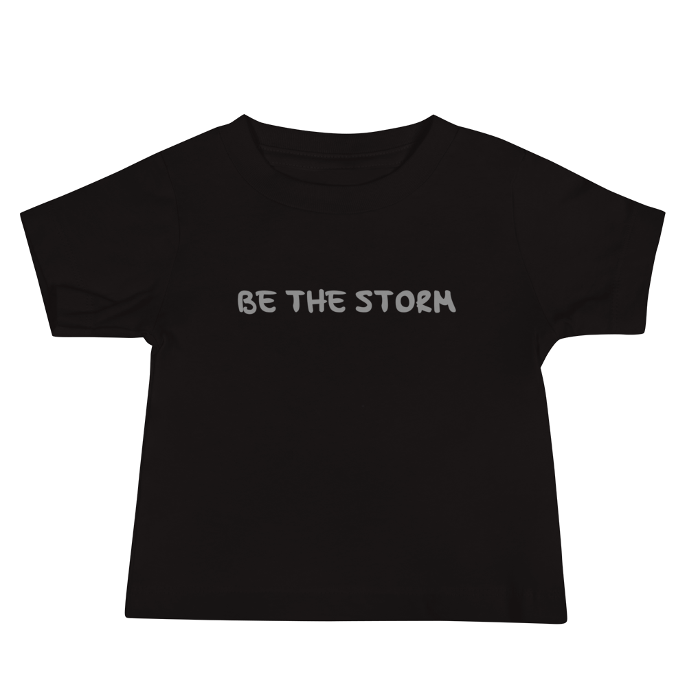 "Be the storm" printed on a black baby jersey short sleeve tee laying on a flat surface