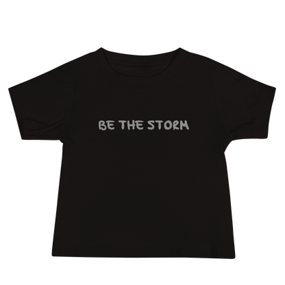 "Be the storm" printed on a black baby jersey short sleeve tee laying on a flat surface