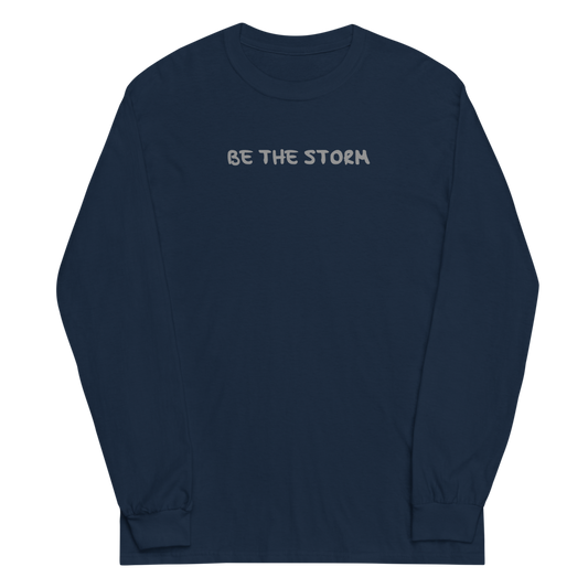 "Be the storm" printed on a navy men's long sleeve shirt laying on a flat surface