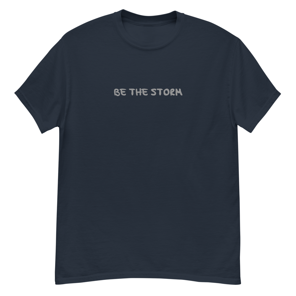 "Be the storm" printed on a navy unisex classic tee laying on a flat surface