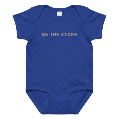 "Be the storm" printed on a royal baby jersey bodysuit laying on a flat surface amongst other clothes