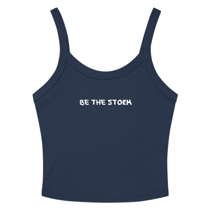 "Be the storm" printed on a solid navy blend women's micro-rib tanktop laying on a flat surface amongst sunglasses and shorts