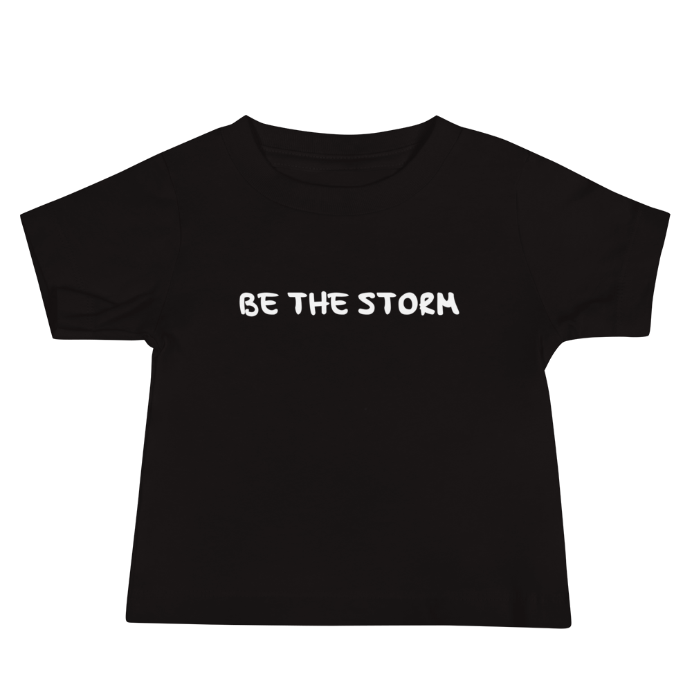 "Be the storm" printed on a black baby jersey short sleeve tee laying on a flat surface