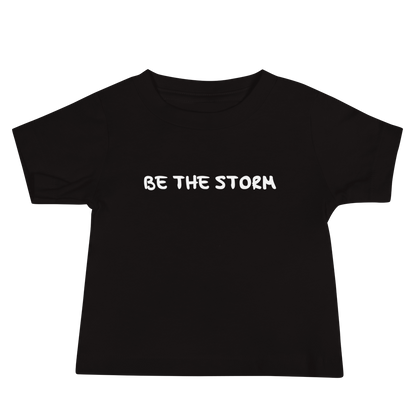 "Be the storm" printed on a black baby jersey short sleeve tee laying on a flat surface