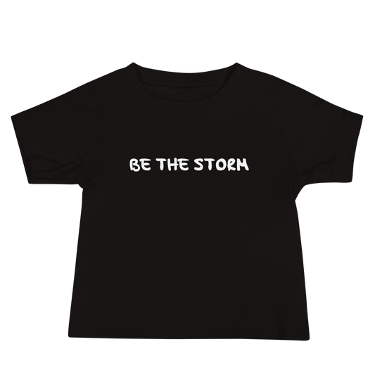 "Be the storm" printed on a black baby jersey short sleeve tee laying on a flat surface