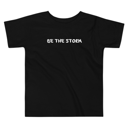 "Be the storm" printed on a black toddler short sleeve tee laying on a flat surface