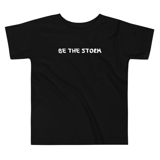 "Be the storm" printed on a black toddler short sleeve tee laying on a flat surface