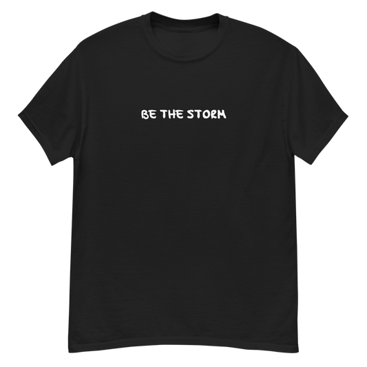 "Be the storm" printed on a black unisex classic tee laying on a flat surface