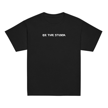 "Be the storm" printed on a black youth classic tee laying on a flat surface