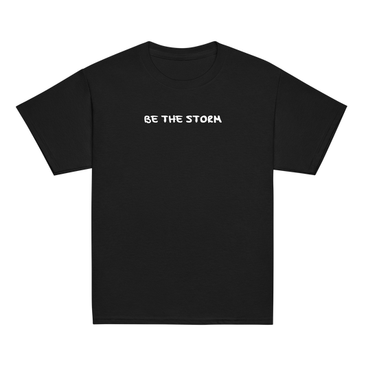 "Be the storm" printed on a black youth classic tee laying on a flat surface