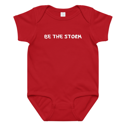 "Be the storm" printed on a red baby jersey bodysuit laying on a flat surface amongst other clothes