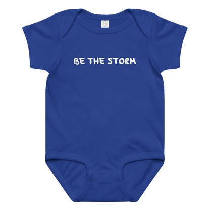 "Be the storm" printed on a royal baby jersey bodysuit laying on a flat surface amongst other clothes