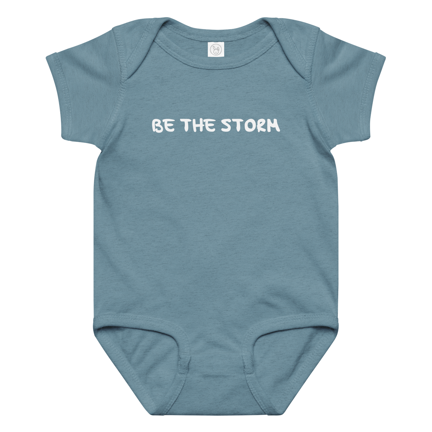 "Be the storm" printed on a vintage indigo baby jersey bodysuit laying on a flat surface amongst other clothes