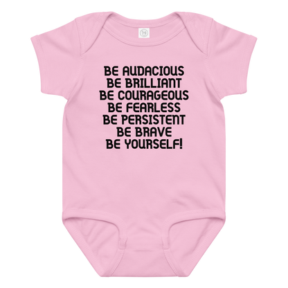 "Be Audacious Be Brilliant Be Courageous Be Fearless Be Persistent Be Brave Be Yourself!" printed on a pink baby jersey bodysuit laying on a flat surface amongst other clothes