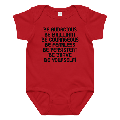 "Be Audacious Be Brilliant Be Courageous Be Fearless Be Persistent Be Brave Be Yourself!" printed on a red baby jersey bodysuit laying on a flat surface amongst other clothes