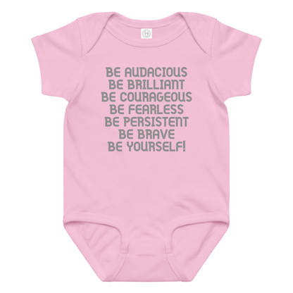 "Be Audacious Be Brilliant Be Courageous Be Fearless Be Persistent Be Brave Be Yourself!" printed on a pink baby jersey bodysuit laying on a flat surface amongst other clothes