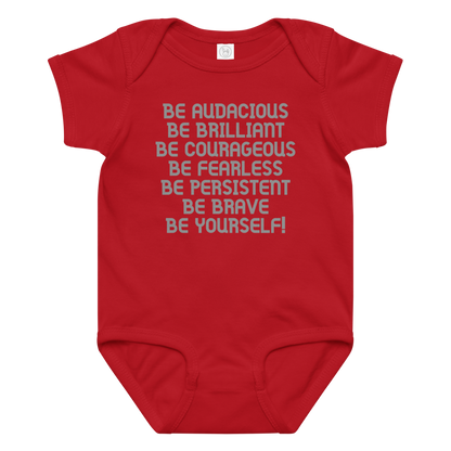 "Be Audacious Be Brilliant Be Courageous Be Fearless Be Persistent Be Brave Be Yourself!" printed on a red baby jersey bodysuit laying on a flat surface amongst other clothes