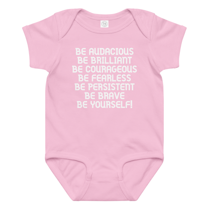 "Be Audacious Be Brilliant Be Courageous Be Fearless Be Persistent Be Brave Be Yourself!" printed on a pink baby jersey bodysuit laying on a flat surface amongst other clothes