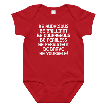 "Be Audacious Be Brilliant Be Courageous Be Fearless Be Persistent Be Brave Be Yourself!" printed on a red baby jersey bodysuit laying on a flat surface amongst other clothes