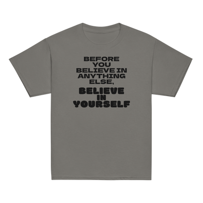 "Before you believe in anything else, believe in yourself" printed on a charcoal youth classic tee laying on a flat surface