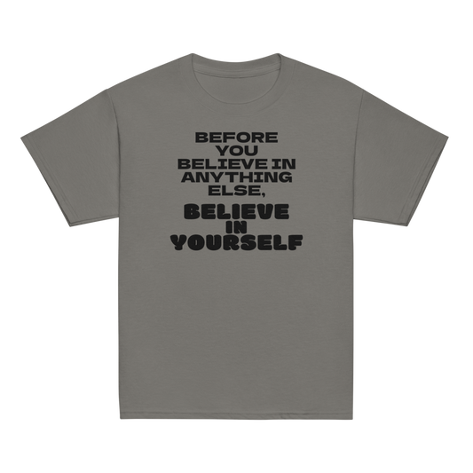 "Before you believe in anything else, believe in yourself" printed on a charcoal youth classic tee laying on a flat surface