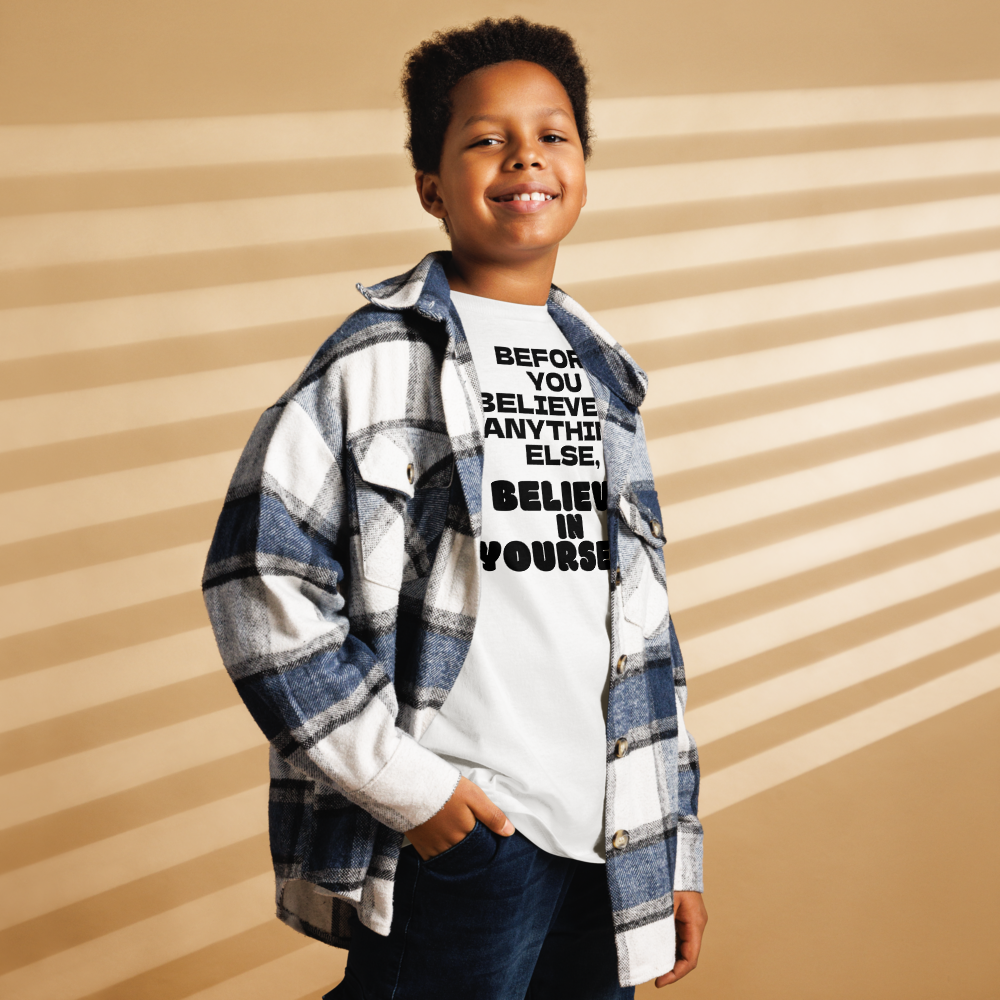 "Before you believe in anything else, believe in yourself" printed on a white youth classic tee worn by a male also wearing a jacket