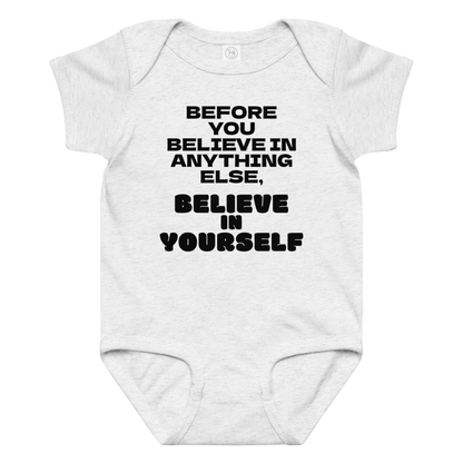 "Before you believe in anything else, believe in yourself" printed on a ash baby jersey bodysuit laying on a flat surface amongst other clothes