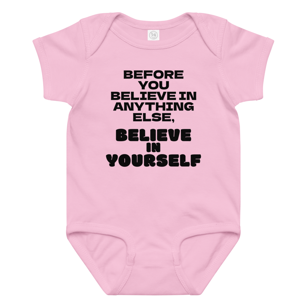 "Before you believe in anything else, believe in yourself" printed on a pink baby jersey bodysuit laying on a flat surface amongst other clothes