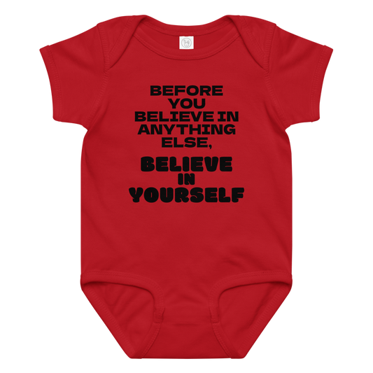 "Before you believe in anything else, believe in yourself" printed on a red baby jersey bodysuit laying on a flat surface amongst other clothes