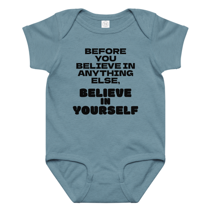 "Before you believe in anything else, believe in yourself" printed on a vintage indigo baby jersey bodysuit laying on a flat surface amongst other clothes